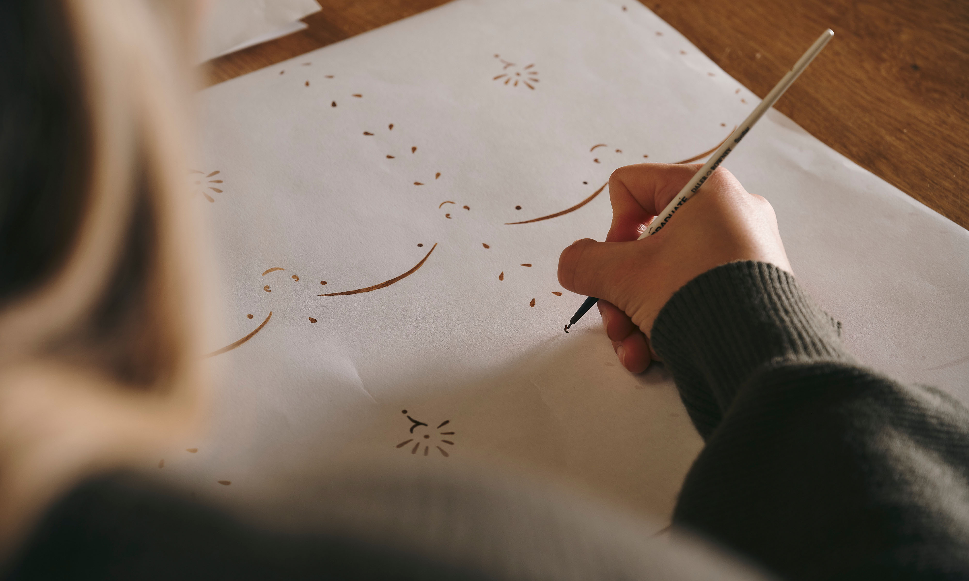 Looking over the shoulder of a woman hand-painting a delicate patterned design.