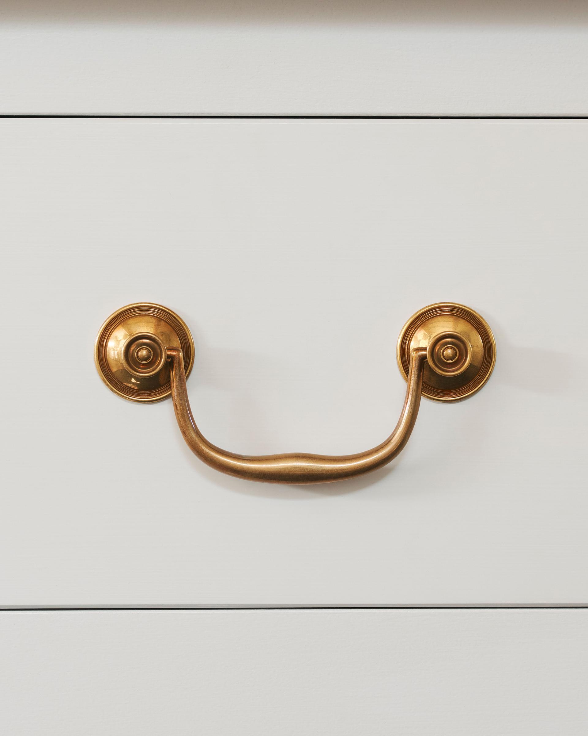 A front-on view of an elegant Georgian-style brass swing handle for kitchen cupboard drawers.