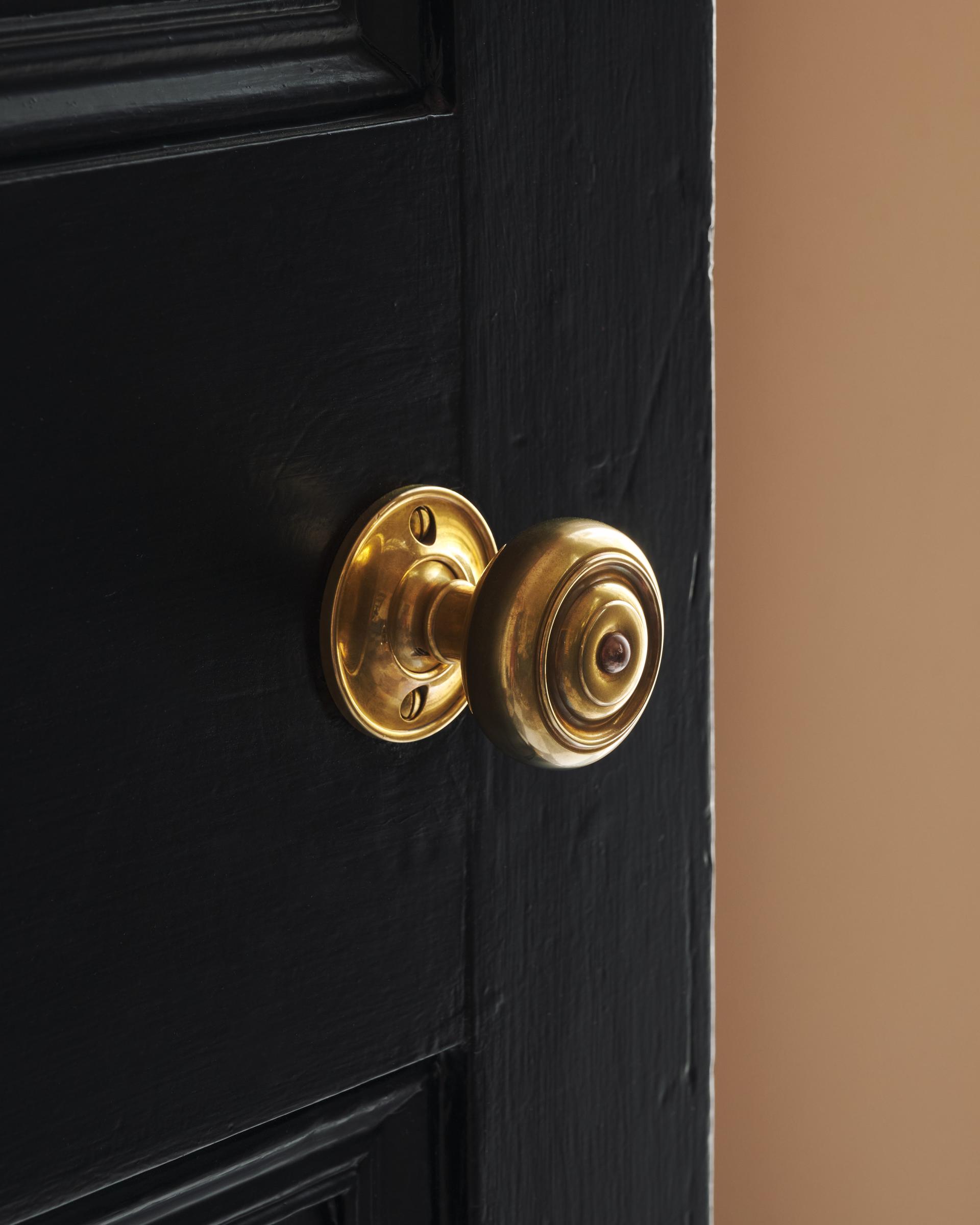 A partial angle of the black door showing the burnished brass knob, capturing its subtle shine against the painted door.