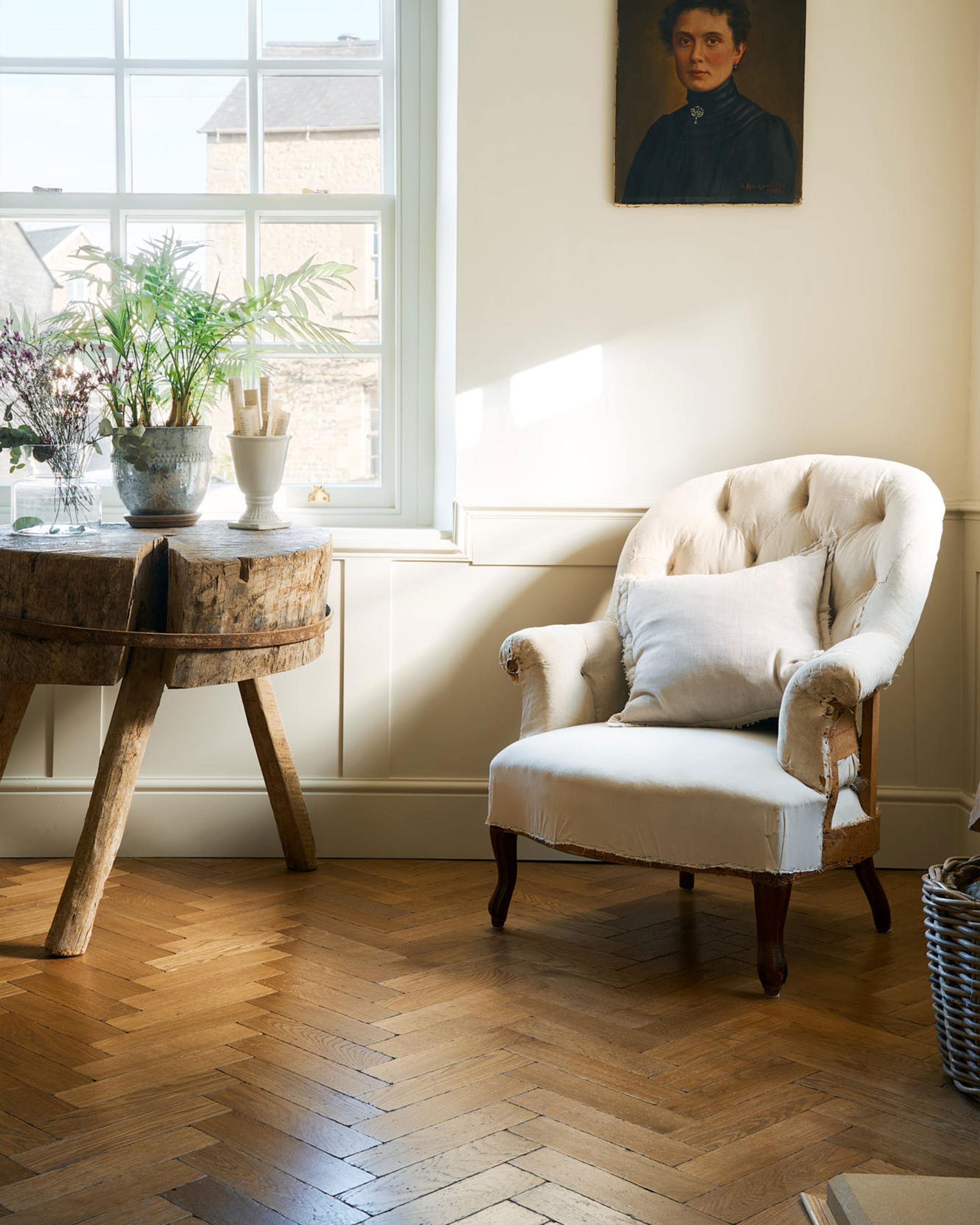 A quiet corner of a modern living room with a vintage wooden side table, a cream armchair, pillow, and the warm wooden Chatsworth Parquet floor.