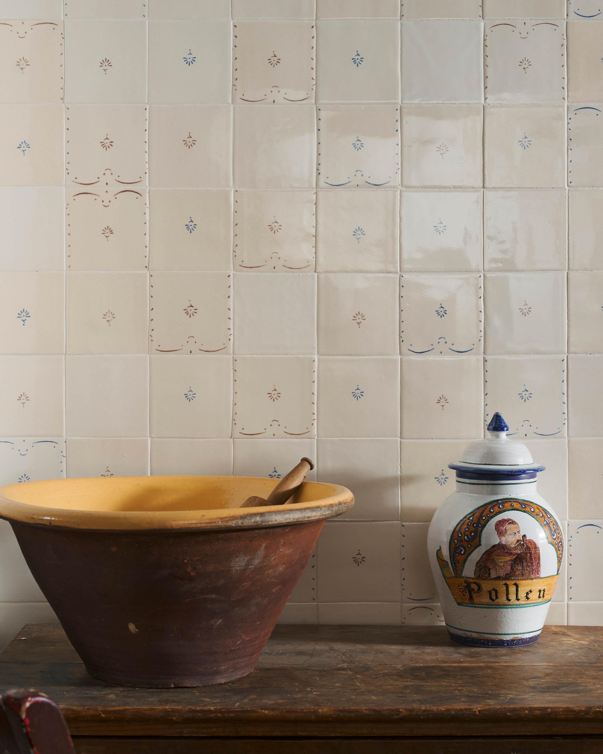 A display of handmade Ditsy Delft Tiles, with a large antique ceramic bowl and painted vase on a wooden table.