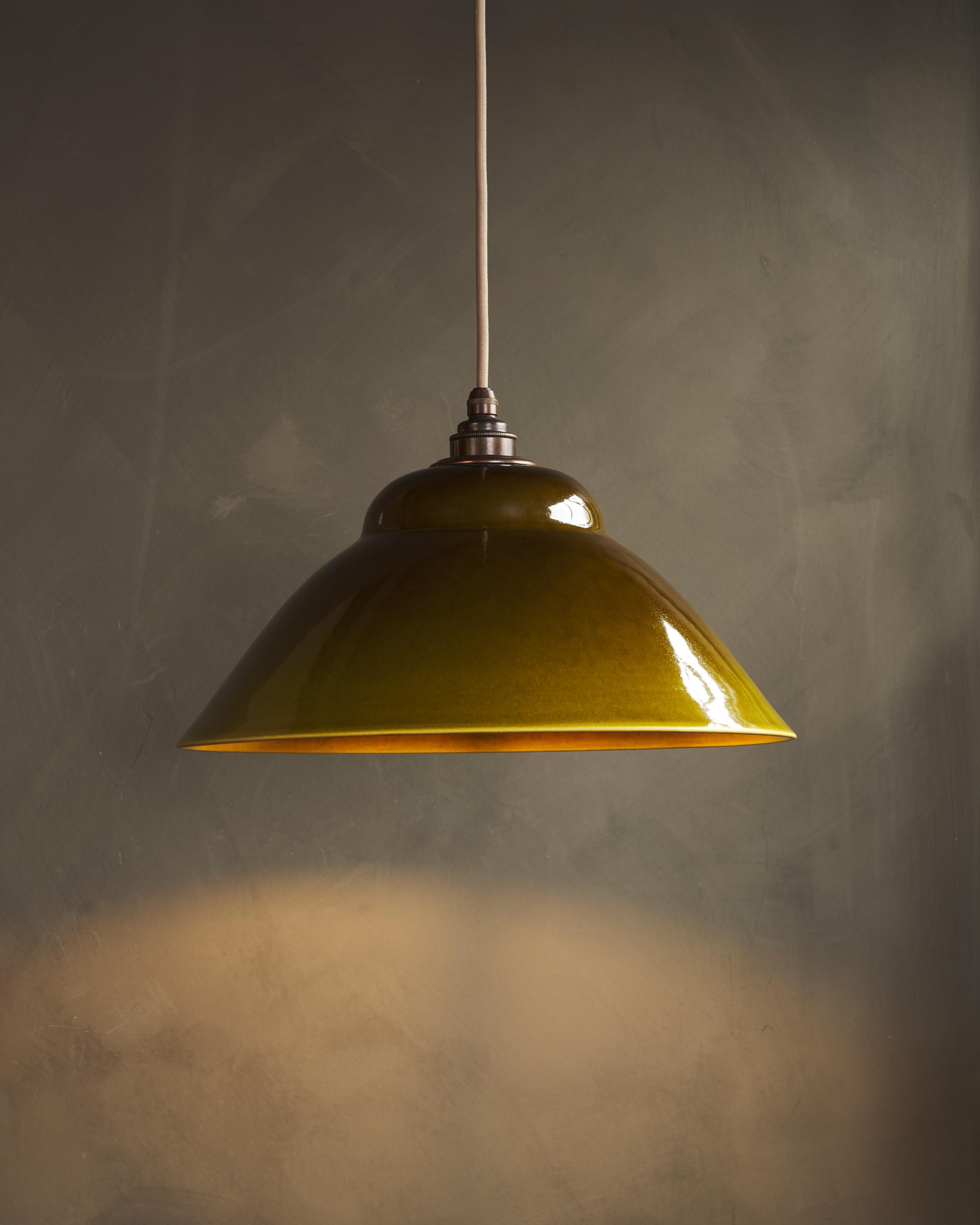 A straight-on view of a mid-century-style sepia glazed ceramic pendant light, the light is on.